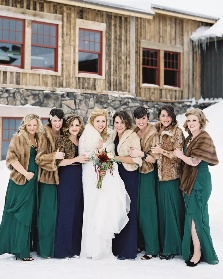 Winter Wedding Guest Attire: Bridesmaids and bride outside of a venue wearing dresses and fur shawls in the snow. 