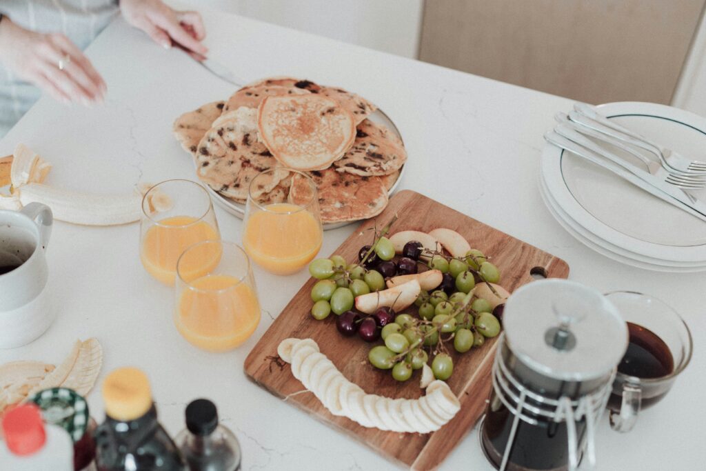 Woman arranging brunch party menu with pancakes, fruit, coffee, and orange juice