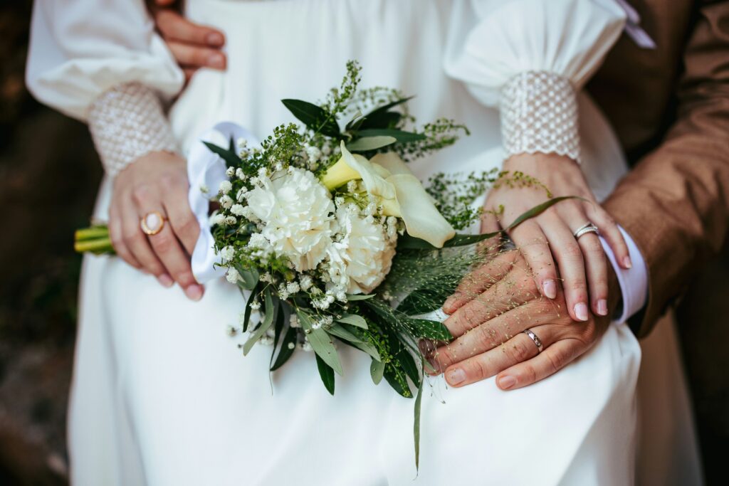 Close-up of a bride holding a bouquet with the groom behind her