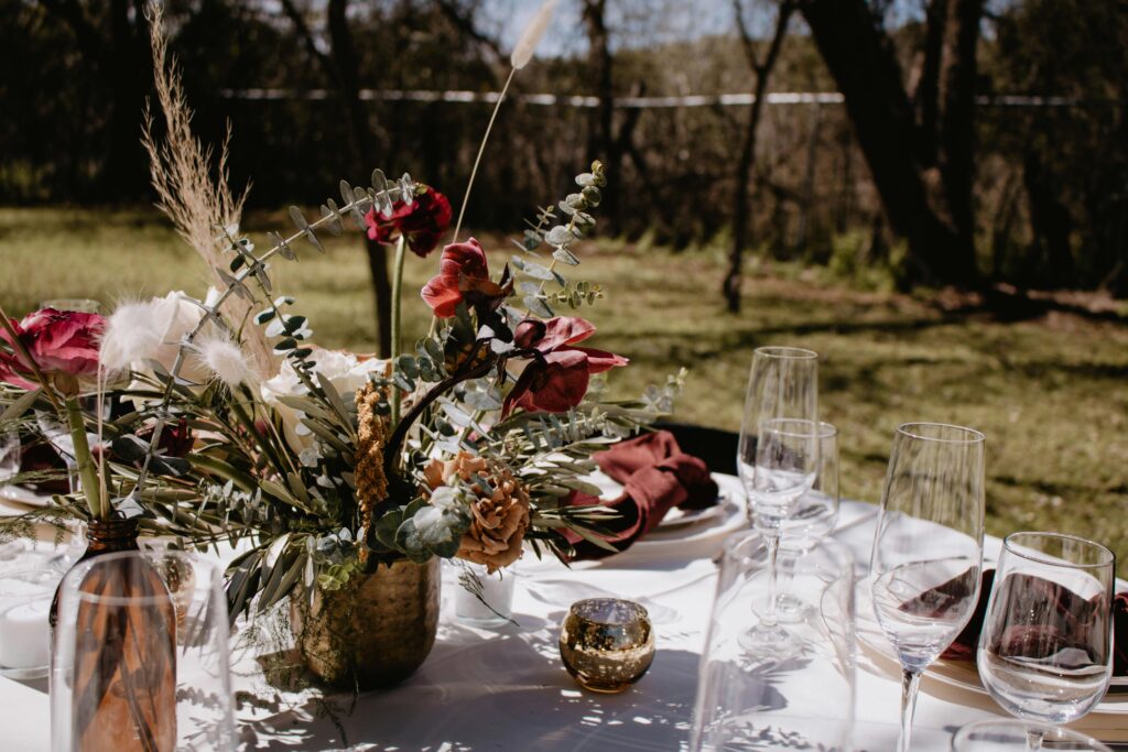 Dried flowers on a table outside with glasses, plates, and silverware