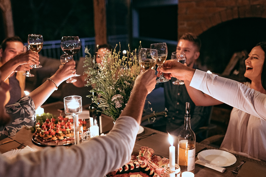 Group of people gathered around a table inside toasting each other with wine glasses in hand