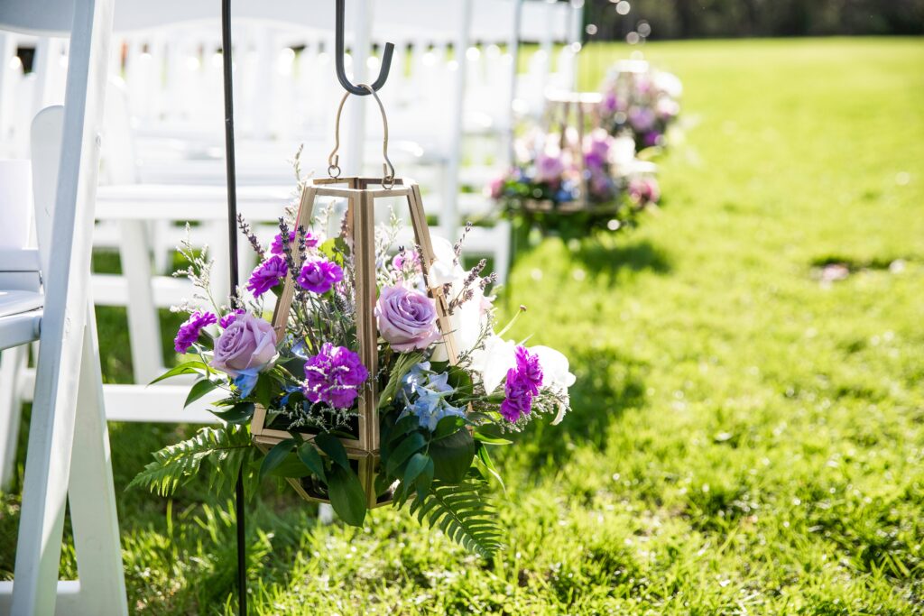 Purple flowers in lanterns lining a wedding aisle outside