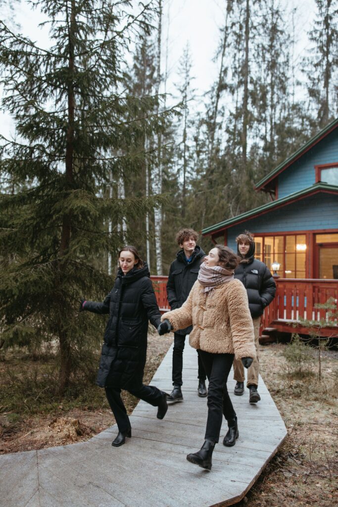 Two women and men walking in the woods by a cabin